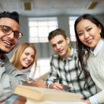 Multi-ethnic group of cheerful students looking at camera and smiling sitting at desk in lecture hall of modern college